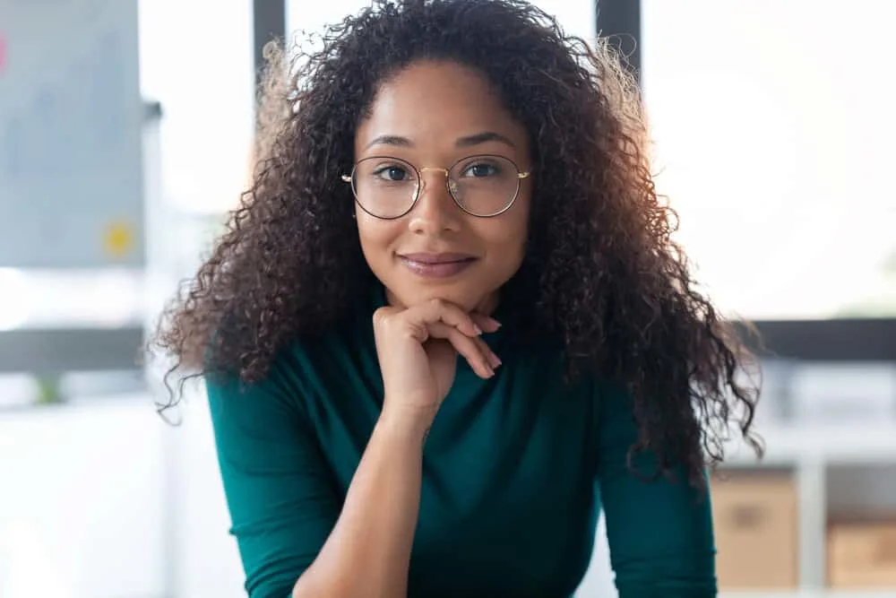 Woman sitting in her office at work with a bad perm with a subtle smile on her face.