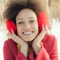 African American woman with kinky knotted hair wearing red earmuffs while chewing gum.