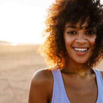 Cheerful African American lady with wavy healthy hair strands with frayed ends walking through the desert.