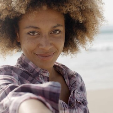 African American woman with a gentle smile wearing blonde bleached hair with dark brown roots.