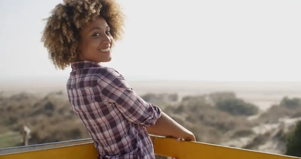 Smiling woman with 4C curls that have been dyed blonde with permanent hair dye.