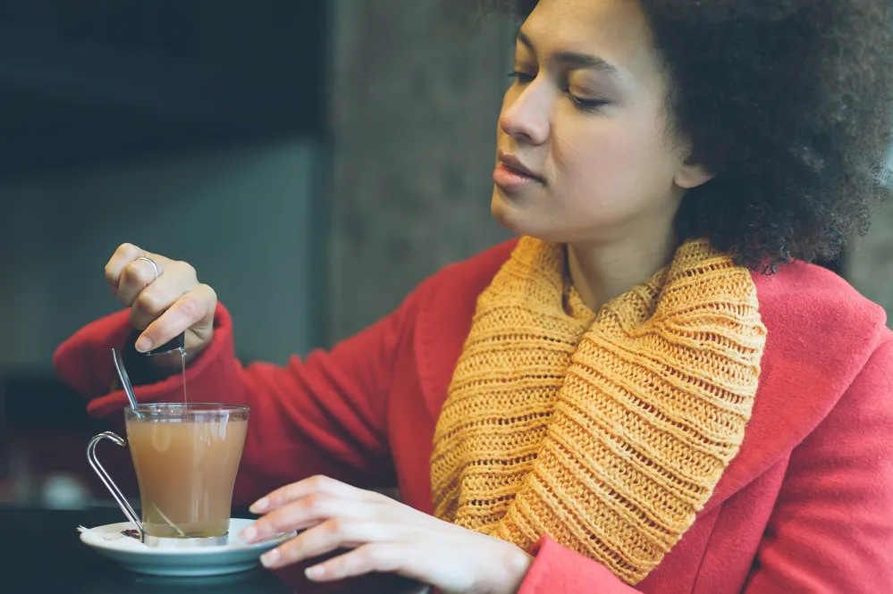 A young lady sipping tea in a restaurant where they've also ordered sticky foods, like sugary granola.