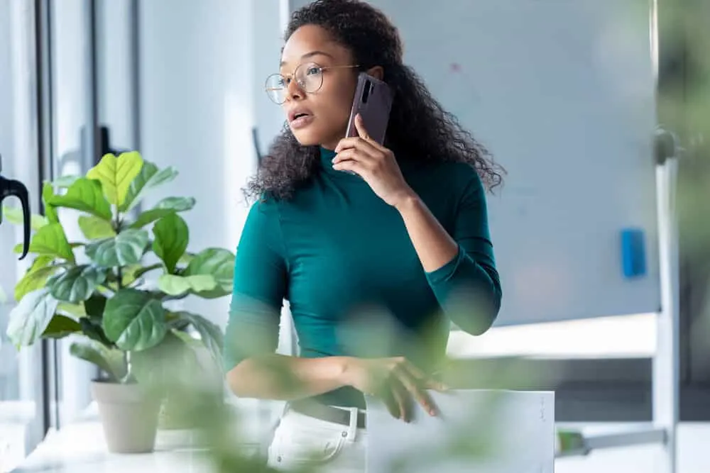 A business woman with curly permed hair on a dark hair color talking on the phone at her workplace.