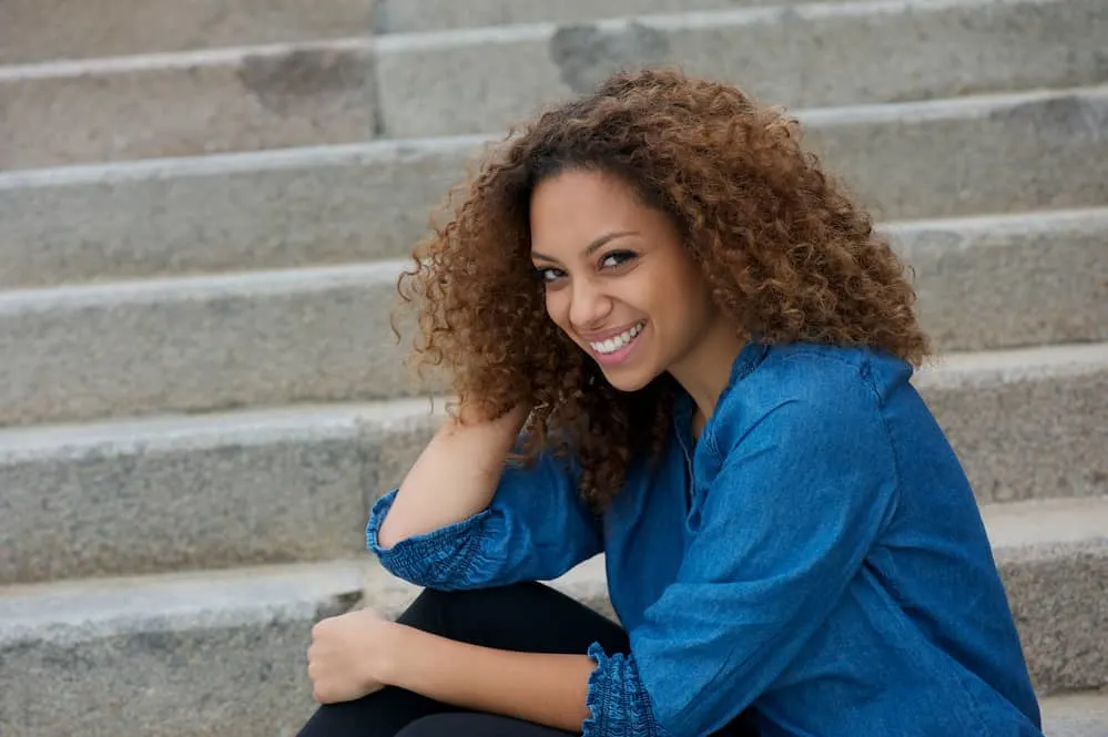 Cute young woman laughing and sitting outside with 3C curls styled in a shadow root hairdo.