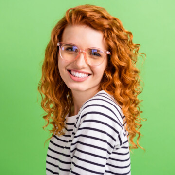 Adorable young woman with wavy bright copper auburn hair wearing a black and white shirt.