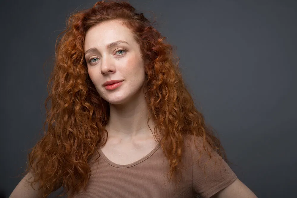 Caucasian female leaving her hair stylist with wavy red hair strands.