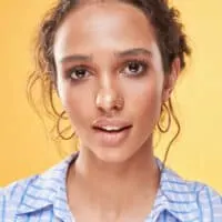 Young black girl with brown frizzy curls wearing a blue plaid shirt dress and hoop earrings