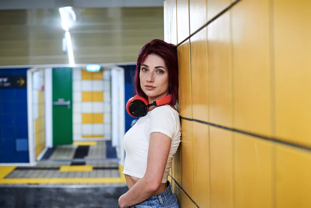 Lady leaning against the wall in a Subway terminal with red and purple mixed hair dye.