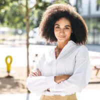 Confident African American with healthy hair standing outside with her arms folded.