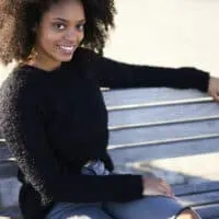 Optimistic African American woman with healthy hair sitting on a bench at the park.