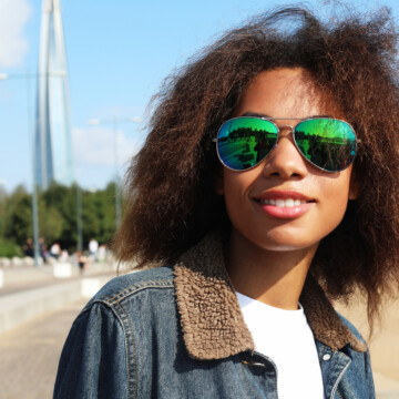 African American female with thick hair sticking up wearing sunglasses and a blue jean jacket.