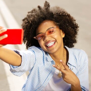 Beautiful young black girl with dark brown hair soaking up the sun's rays while taking a selfie.