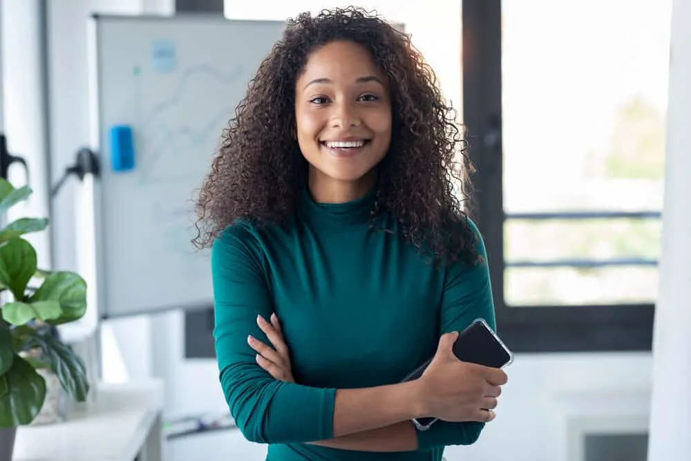 Photo on a black female with natural-looking long hair that got a perm recently is wearing a green shirt.