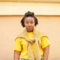 Black girl with dry hair properly dried to avoid a musty smell wearing a yellow t-shirt and sweater tied around her arms.