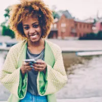 Cheerful woman with curly dark hair styled with permanent Splat hair dye standing near a lake.