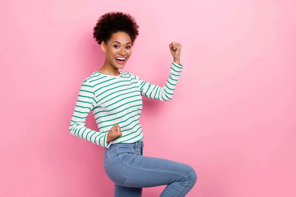 A happy young lady with semi-permanent hair color in her natural curls wearing a green and white shirt.