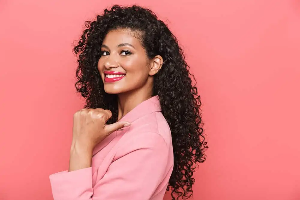 Young female with natural curls dyed dark brown with semi-permanent hair dye wearing a pink business suit.