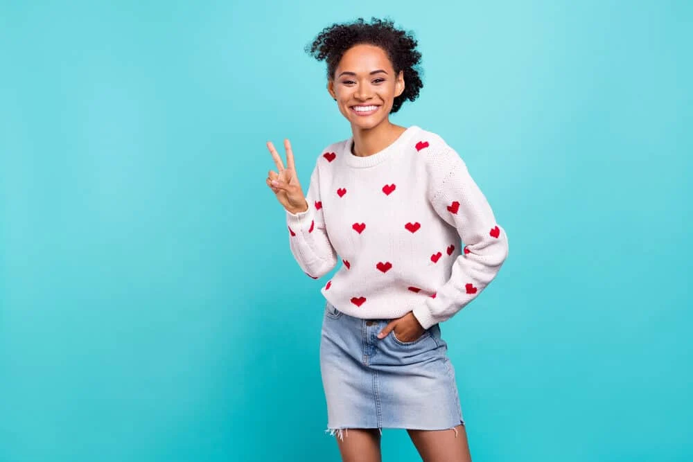 Cute black girl wearing a casual outfit with pastel colours while making a peace sign with her fingers.