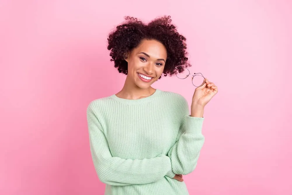 Lady with a strawberry natural shade on 3B curls wearing round glasses and pink lipstick.