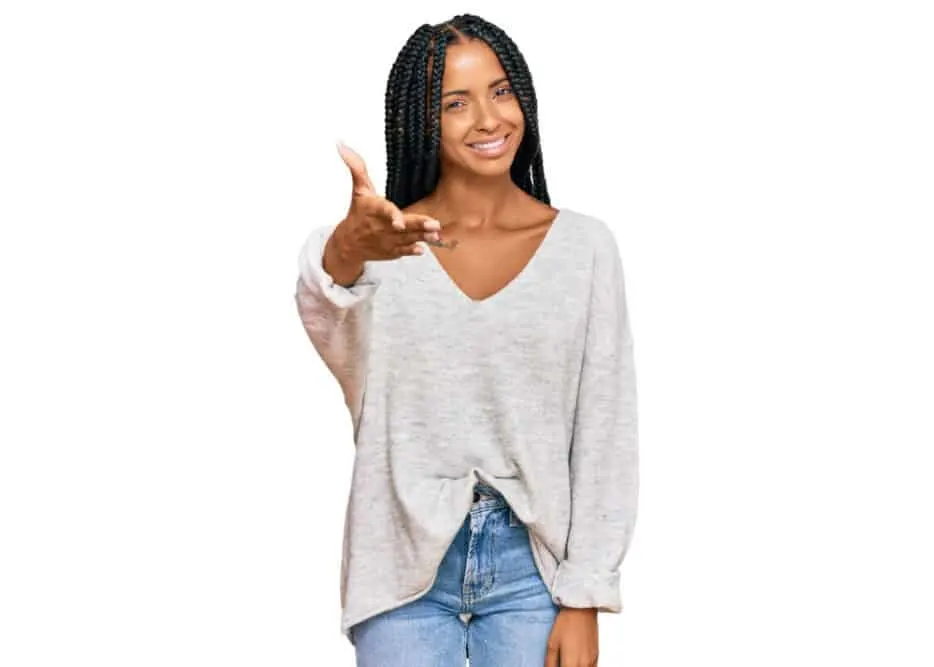 Cute Hispanic woman with short braids wearing a light brown sweater and blue jeans.