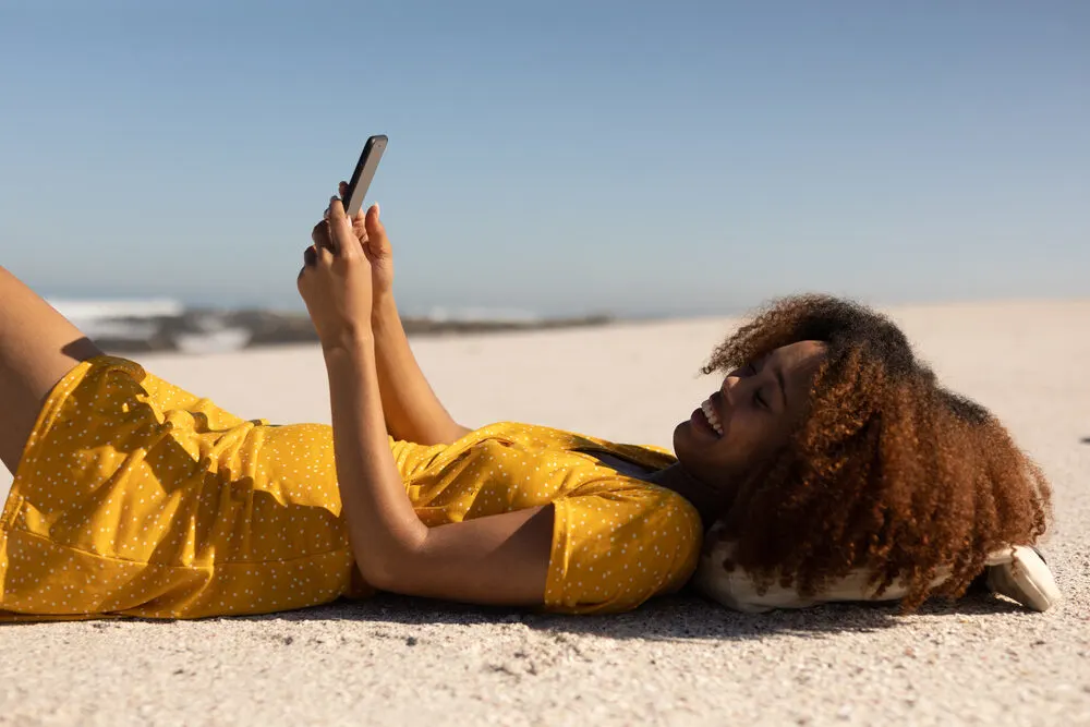 A lady relaxing on the beach wearing strip lashes and a twist-out hairstyle on natural 3C curls.