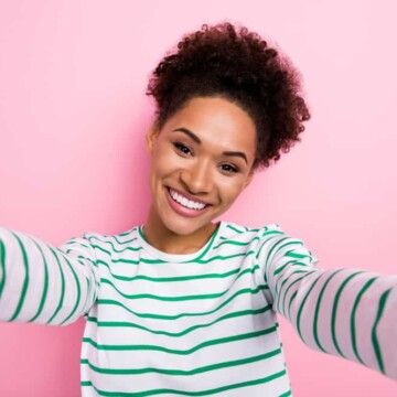 Cute black lady with a dark brown natural hair color with curly hair strands wearing a green and white shirt.