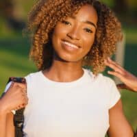 African American female wearing a white t-shirt with light brown dyed hair on naturally black hair.