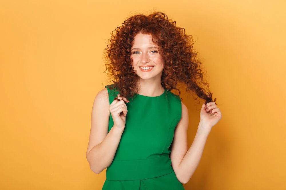 Cute Caucasian female with 1C hair with curls after a perm showing off her new curly texture holding a few strands.