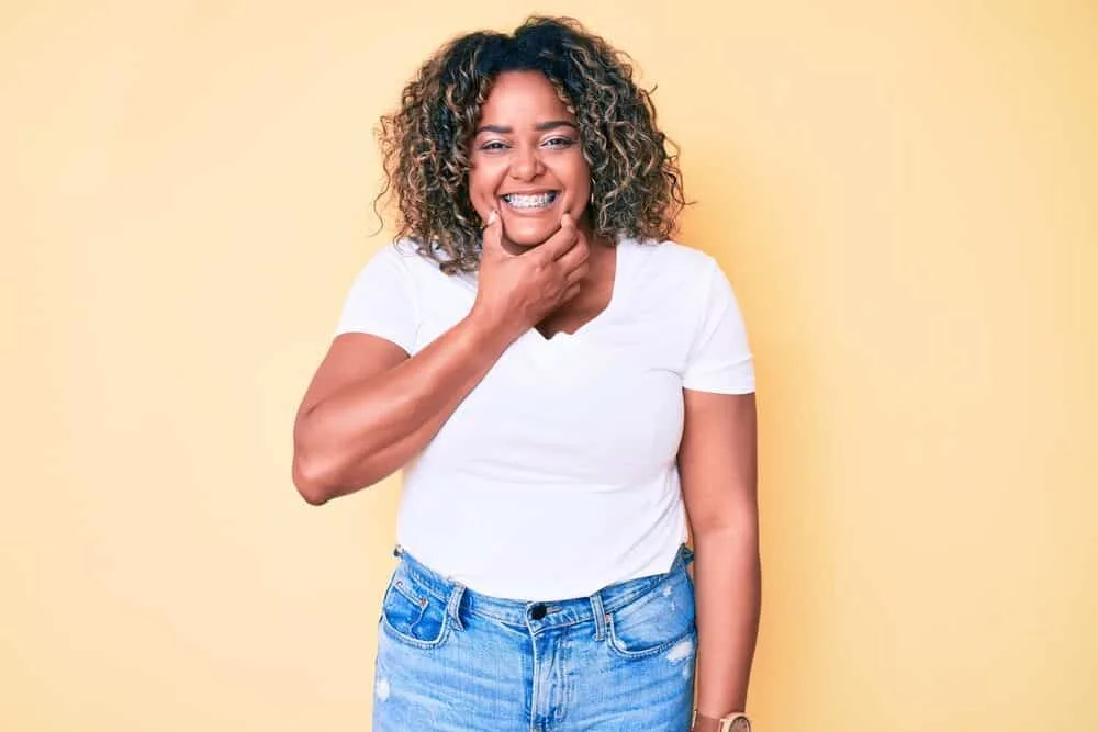 American female with a big smile and demi-permanent color-treated hair wearing a curly hairdo. 