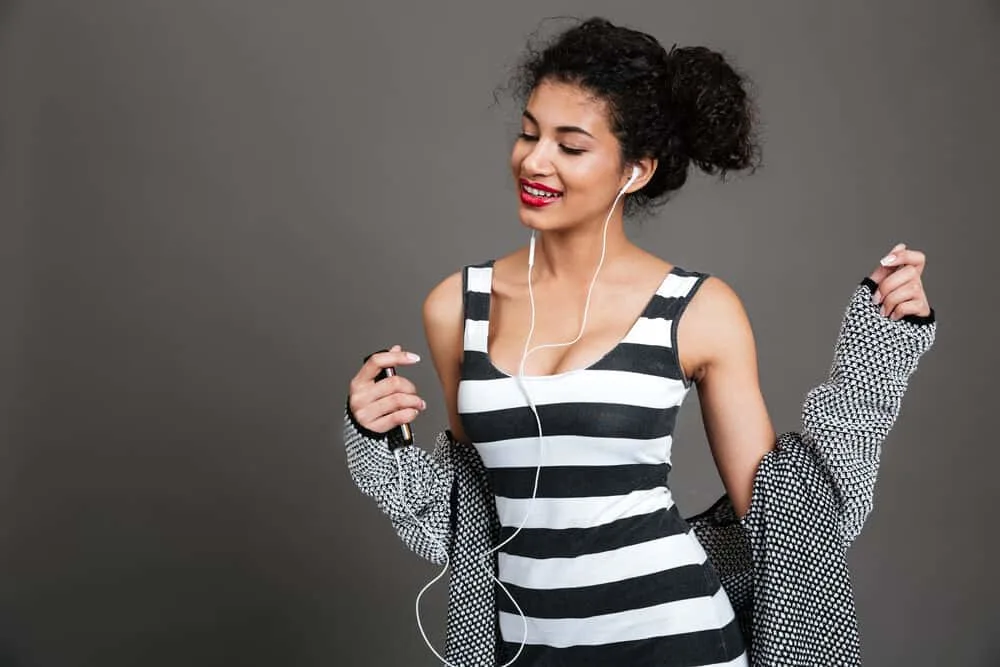 A black woman with natural curls styled with fresh aloe vera gel from the aloe vera leaf listening to music.