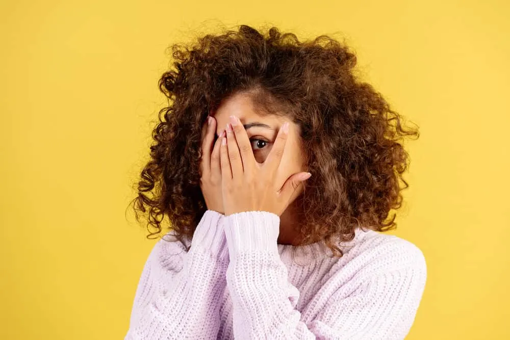 A black woman with her face covered with her hands wearing dark brown 3B naturally curly hair.