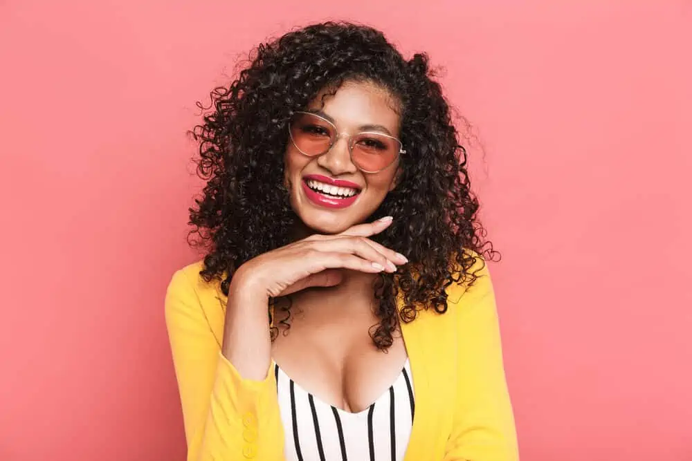 Lovely African female wearing a low-maintenance hairdo with a yellow jacket and pink-tinted glasses.