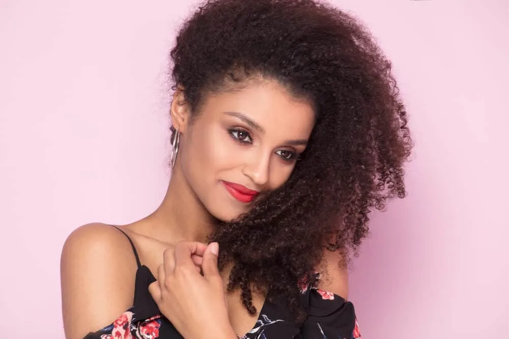 African American woman with dark brown color services on 3C curly hair wearing a rose-colored dress.