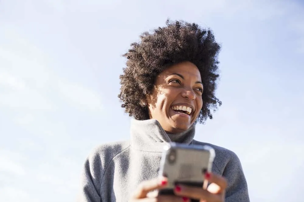 Cute black girl with beautiful skin and hair using an iPhone to text a friend in the park. 