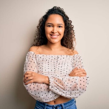 A beautiful woman with a deva hair cut wearing her curly natural hair with a black and white satin shirt.