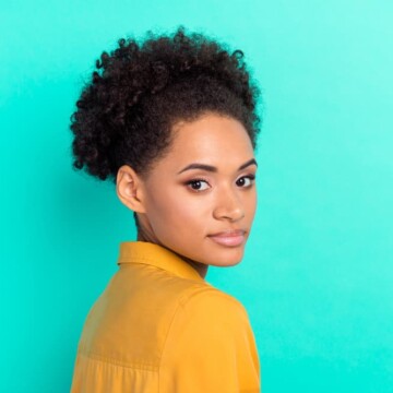 An attractive African American female with healthy hair wearing natural make-up and a yellow dress shirt.