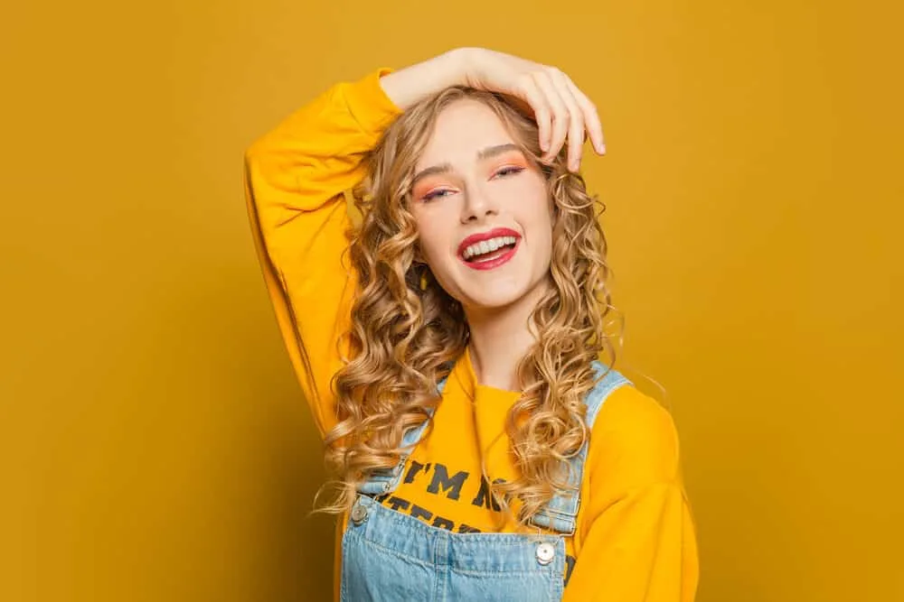 Caucasian white girl with naturally blonde hair that's turning dark brown wearing a yellow shirt with overalls.