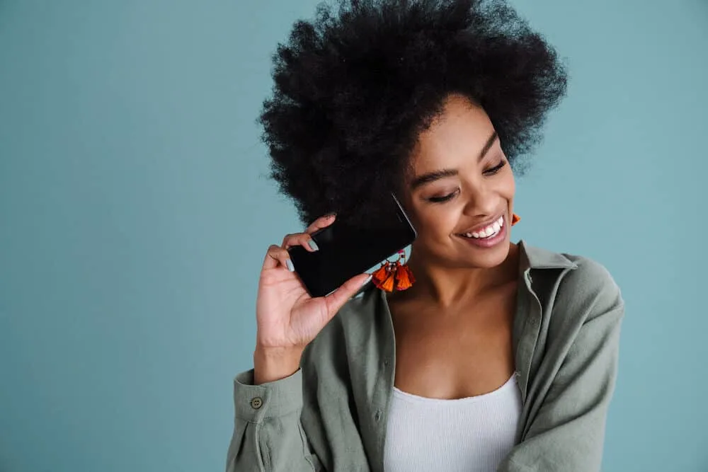 A woman with natural black hair talking to a friend on her cell phone.