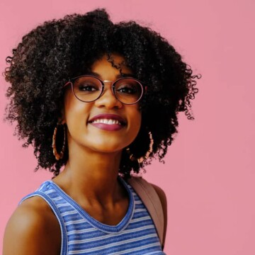 Cute African American female with a full head of curly thick hair strands wearing black eyeglasses.