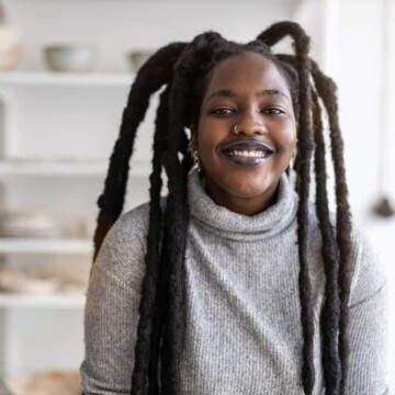 African American female with semi-freeform dreads wearing a gray sweater and black lipstick.