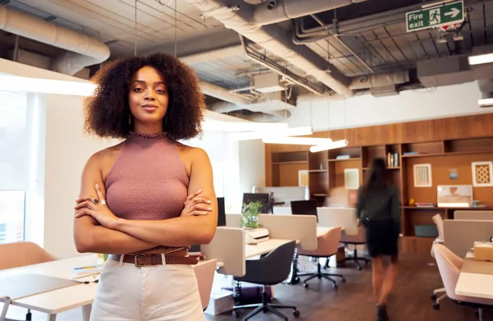 A confident lady wearing 3A natural curls with a purple shirt and white pants in an office building. 