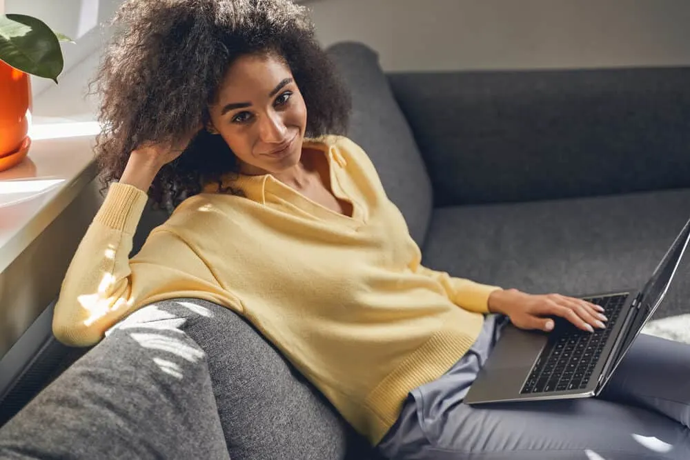 A lady wearing a yellow sweater with fine hair using a laptop to research good hair habits and good hair care tactics.