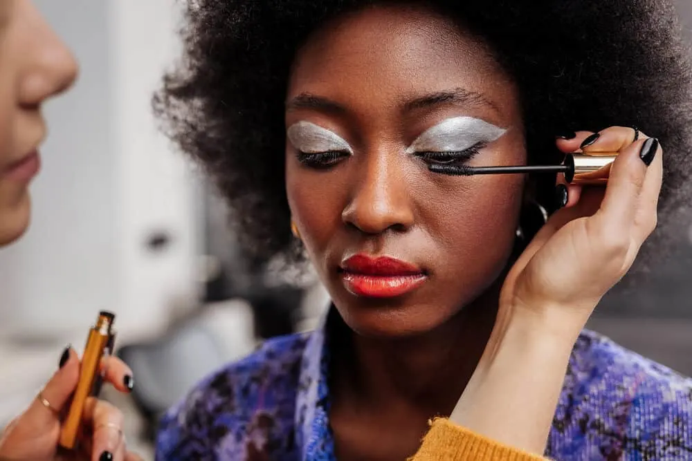 A young black girl with thicker hair styled with curl cream is getting her makeup done professionally.