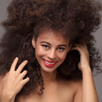 Cute African American female wearing a synthetic wig gently styled and combed with a wig brush.