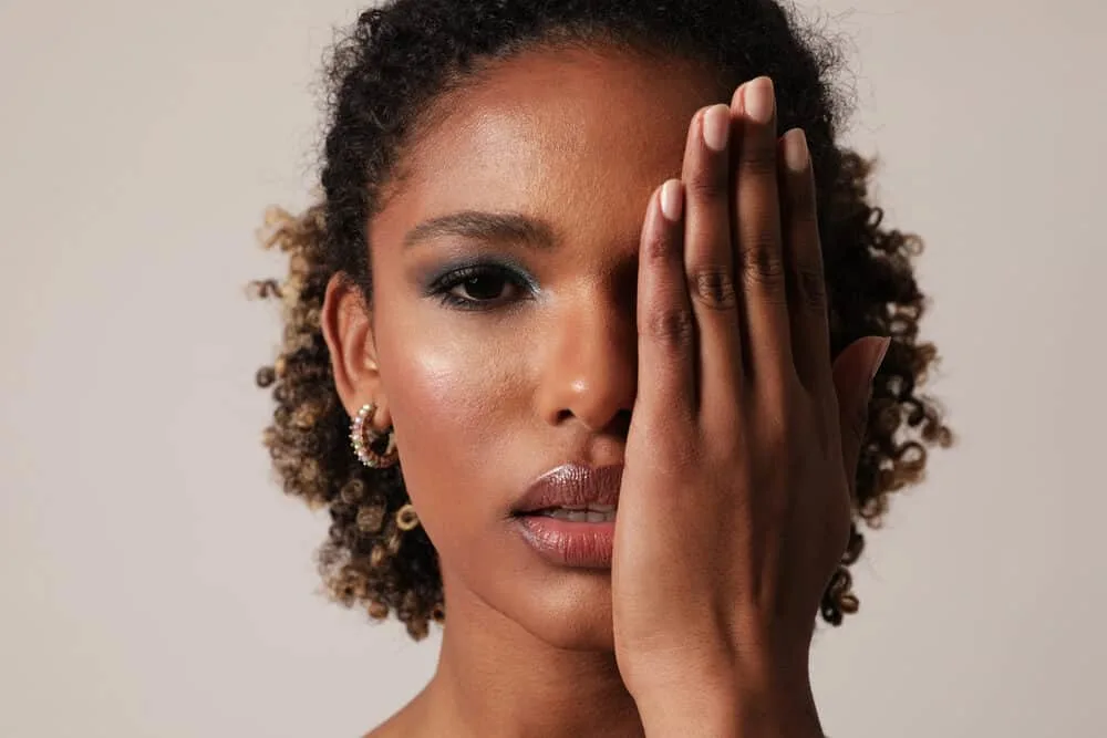 Cute young woman wearing her freshly washed clean hair in a curly ponytail while covering her left eye.