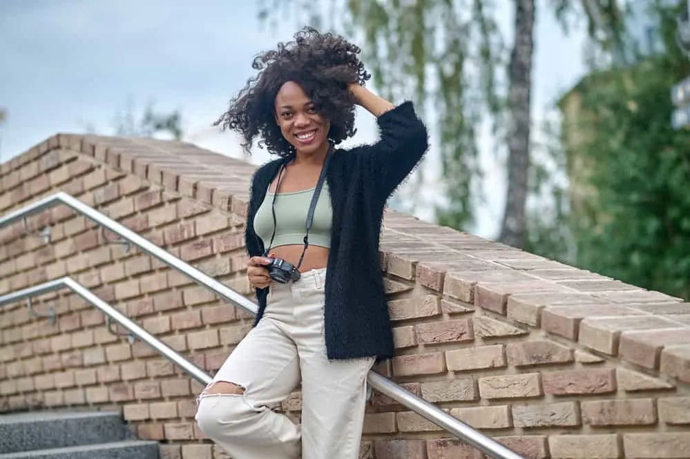 African American girl wearing a curly lace front made from real hair standing outside in direct sunlight taking photos.