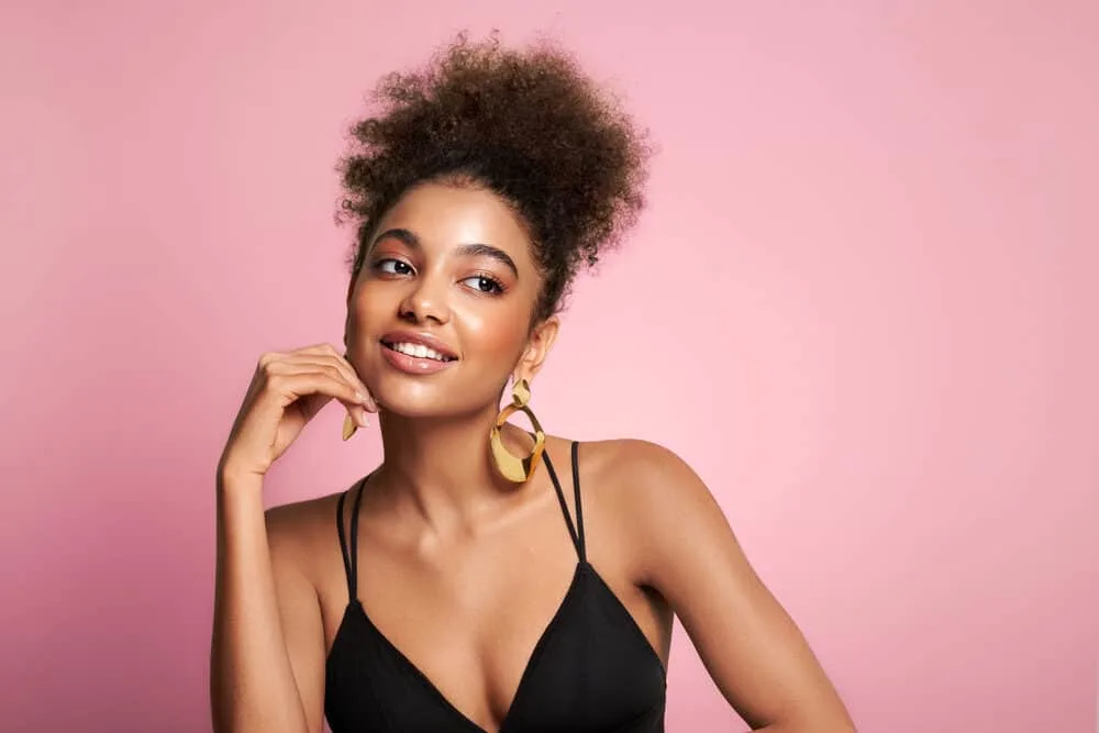 Pretty female with a black natural hair color wearing gold earrings, pink lipstick, and a black evening gown.