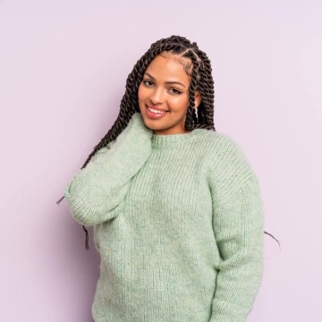 Mexican female mixed with African descent with thick hair in medium braids wearing a green sweater.