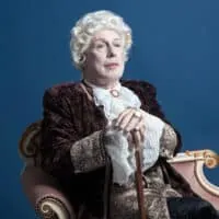 An older Caucasian man dressed as King Louis XIV wearing a human hair wig with white hair covering his own hair.