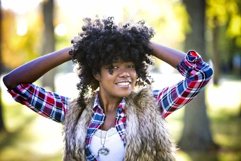 A cute black girl with thin natural hair wearing an artificial hairpiece covering her own curly hair strands.